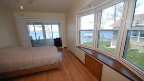 A bedroom with a bed, a window with a view of the water, and a sliding door leading to a balcony. - Lake House with Sandy Beach and Amazing Sunsets (Delton)