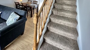 A staircase with wooden balusters leading to a second floor, a dark-colored sofa with a patterned pillow, and a ceiling fan in a living room area. - Beautiful updated condo w modern decor, overlooking Fenwick lighthouse from deck (Ocean City)