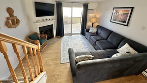 A living room with a fireplace, a sofa, a television, and a staircase. - Beautiful updated condo w modern decor, overlooking Fenwick lighthouse from deck (Ocean City)