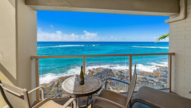 A balcony with a table and chairs overlooking a rocky beach and the ocean. - Spectacular Oceanfront Corner Unit Condo at Kuhio Shores (Koloa)