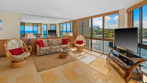 A spacious living area with a large TV, comfortable seating, and a view of the ocean. - Spectacular Oceanfront Corner Unit Condo at Kuhio Shores (Koloa)