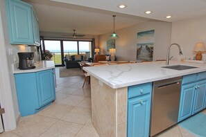 A kitchen with blue cabinets, a marble countertop, and a view to the outside.