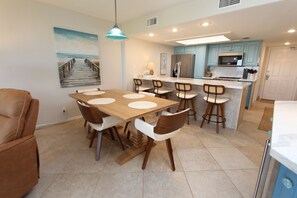 A modern kitchen with a central island, wooden dining table, and bar stools.