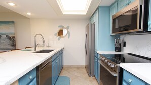 A modern kitchen with blue cabinets, stainless steel appliances, and a skylight. - Seas Life's Moments - Condo 202: Spacious 2BR retreat in South Padre Island, sleeps 7. (South Padre Island)