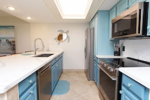 A modern kitchen with blue cabinets, stainless steel appliances, and a skylight. - Seas Life's Moments - Condo 202: Spacious 2BR retreat in South Padre Island, sleeps 7. (South Padre Island)