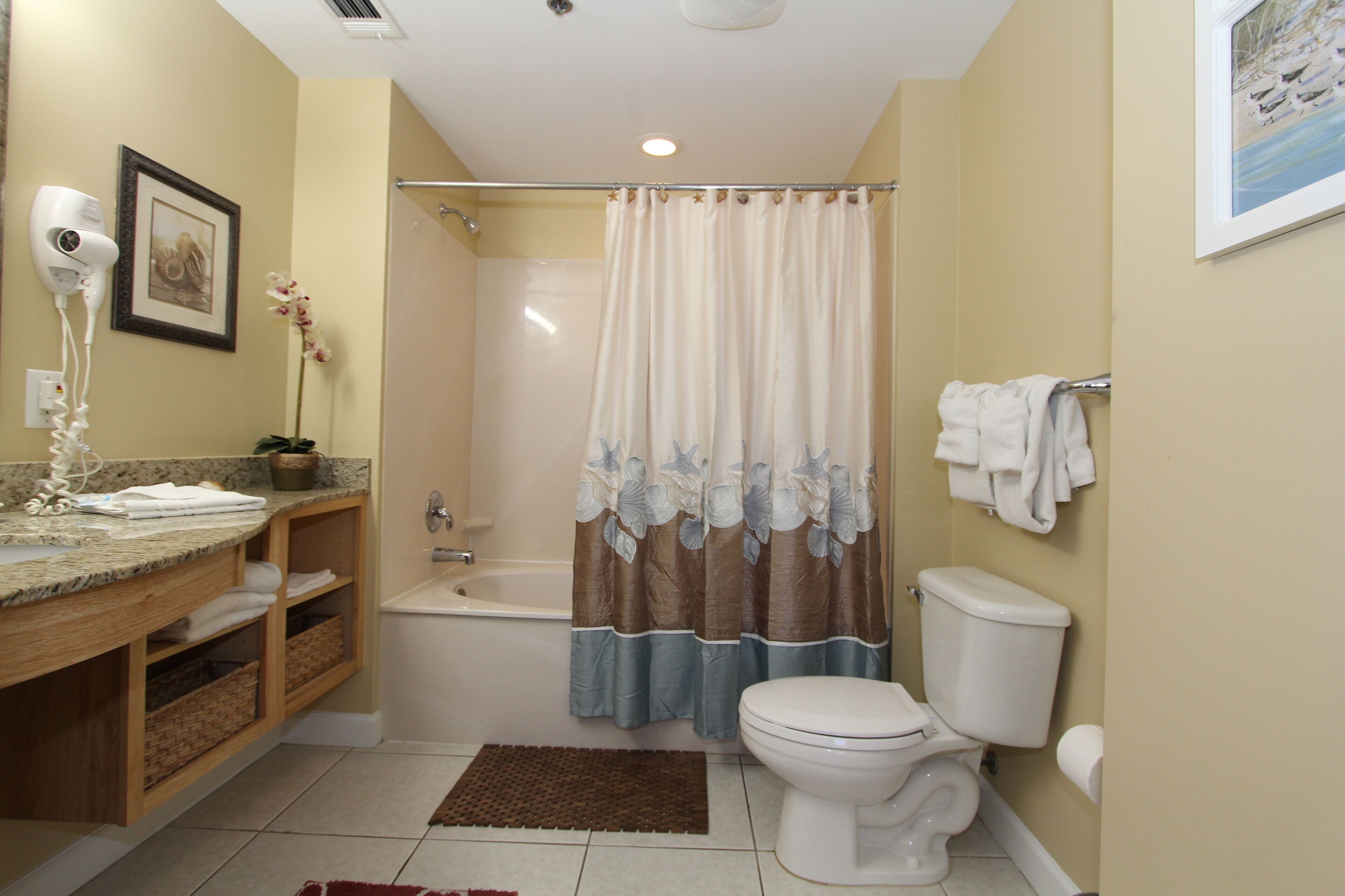 A bathroom with a shower, toilet, sink, and a hairdryer on the wall.