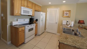 Cocina compacta con armarios de madera, microondas, refrigerador, estufa y pileta.