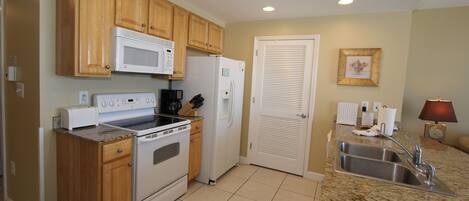 A compact kitchen with wooden cabinets, a microwave, a refrigerator, a stove, and a sink.