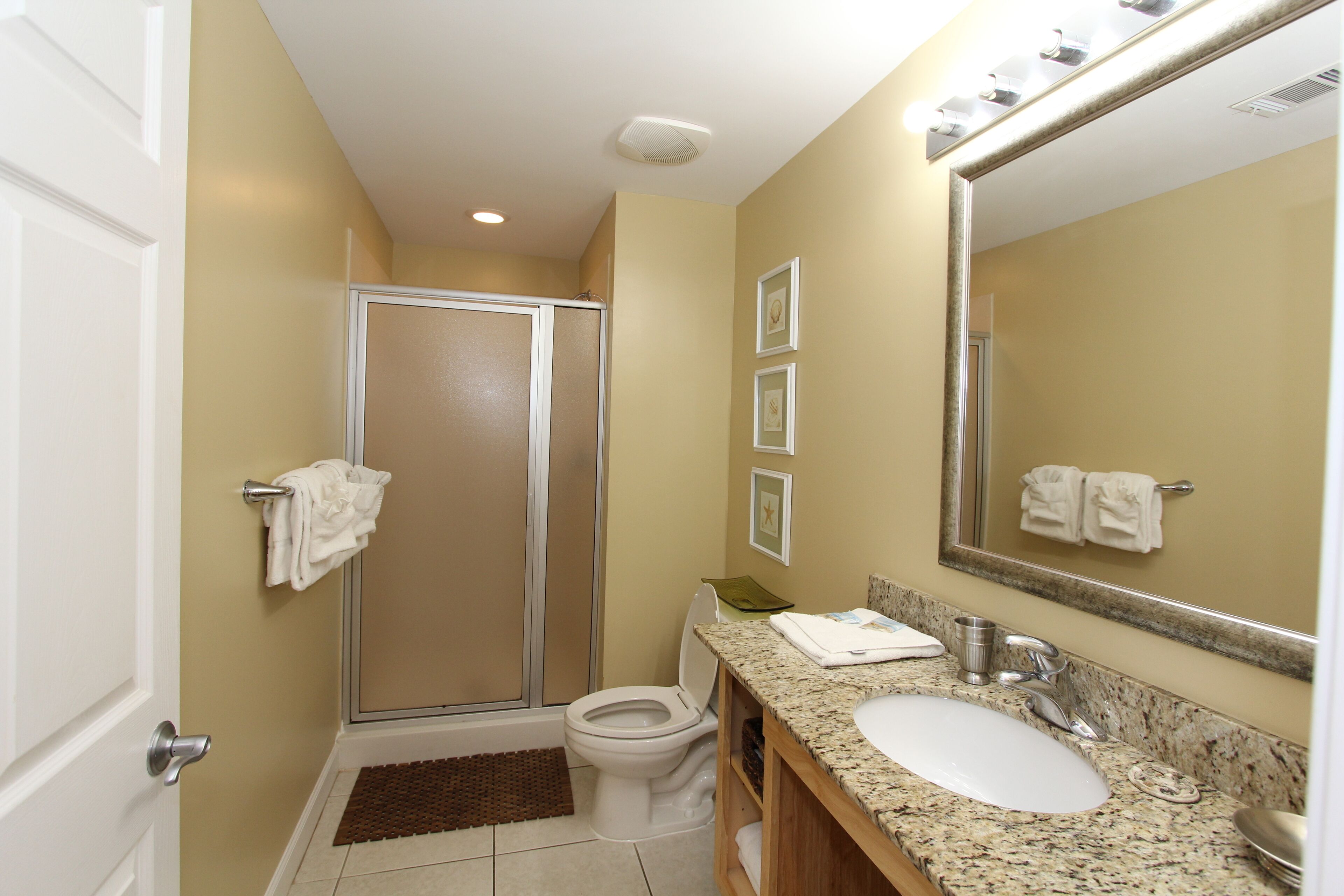 A bathroom with a shower, toilet, sink, and a large mirror.