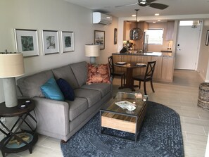 A modern living room with a grey sofa, a glass coffee table, and a dining area with a wooden table and chairs.