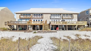 A beachfront building with multiple balconies, a sandy walkway, and outdoor seating areas.