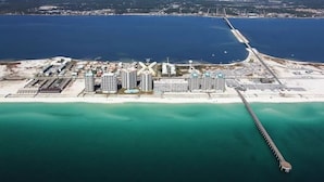 An aerial view of a coastal area with a long pier extending into the water, surrounded by high-rise buildings and a sandy beach.