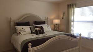 A neatly made bed with a headboard, a bedside table with a lamp, and a window with blinds. - 2 BED/2BATH PLUS DEN  COURTYARD VILLA (The Villages)