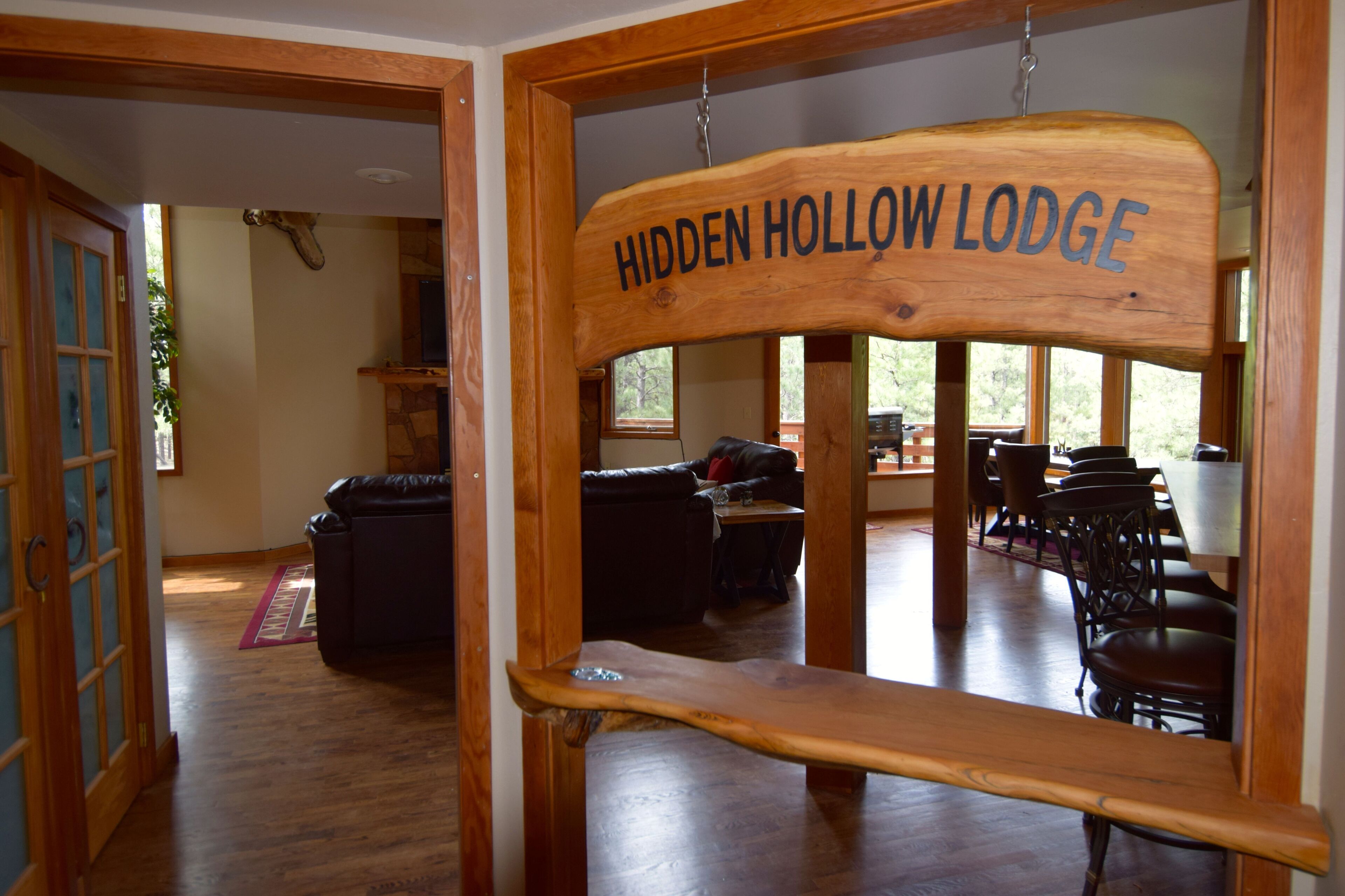 Puinen kyltti, jossa lukee ”Hidden Hollow Lodge”, on sijoitettu viihtyisän mökin sisätiloihin, joissa on ruokailutila ja oleskeluhuone.