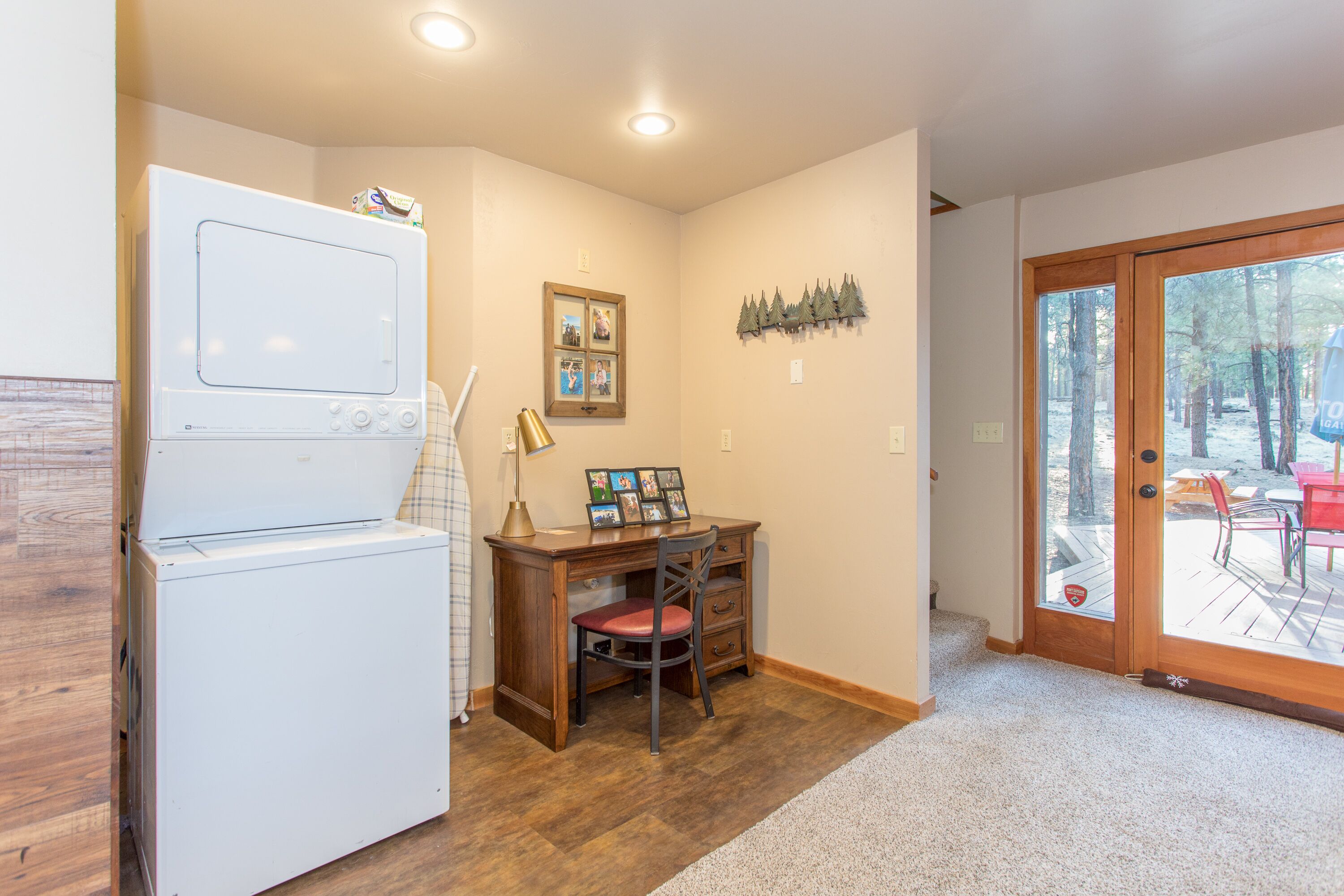 A compact kitchen with a built-in washer and dryer, a wooden desk with a chair, and a glass door leading to an outdoor deck.