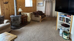 Een gezellige woonkamer met een houtkachel, een bank, een televisie en een boekenkast.