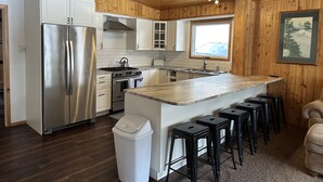 Een moderne keuken met houten lambrisering, roestvrijstalen apparatuur, een centraal eiland met barkrukken en een raam dat natuurlijk licht toelaat.