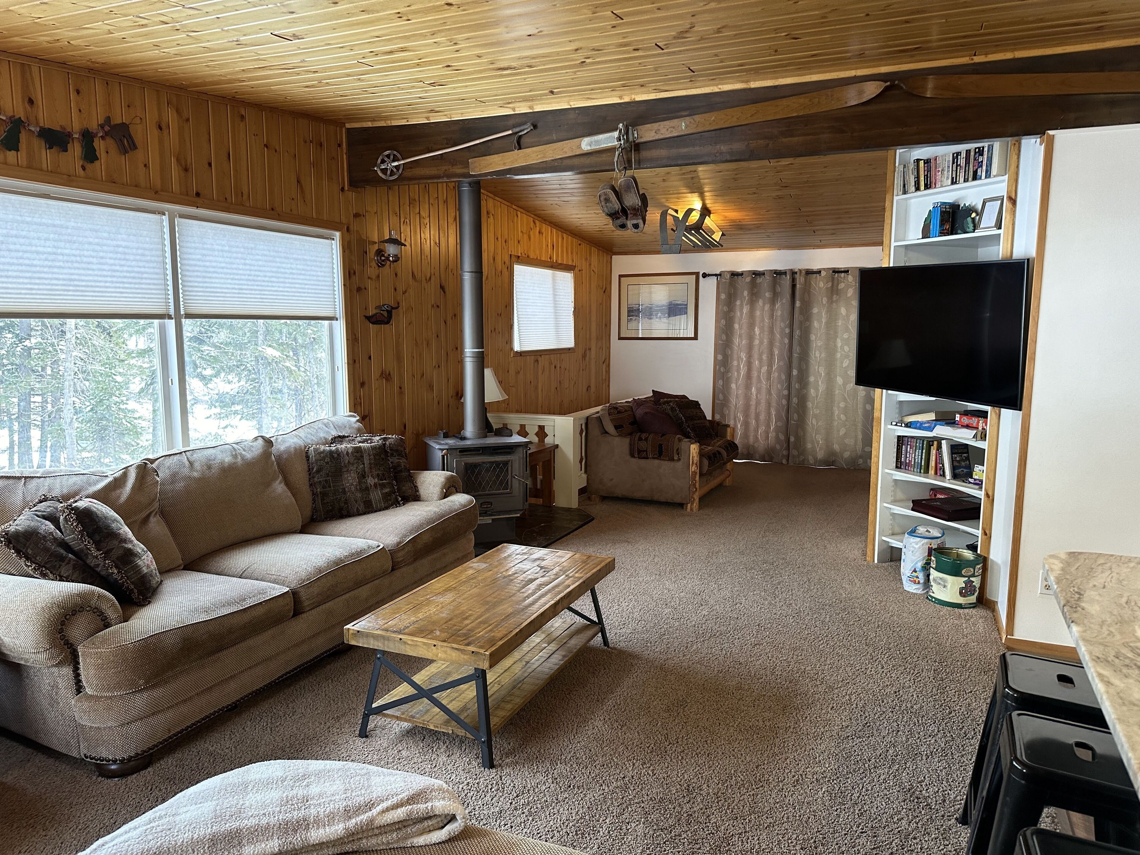 A cozy living room with a wooden ceiling, a sofa, a coffee table, a fireplace, a television, and a bookshelf.