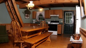 A rustic kitchen with wooden cabinets, a stove, and a dining area with a wooden table and chairs. - Getaway Cabin next door to Maramec Spring Park & Meramec River Trophy Trout (St James)