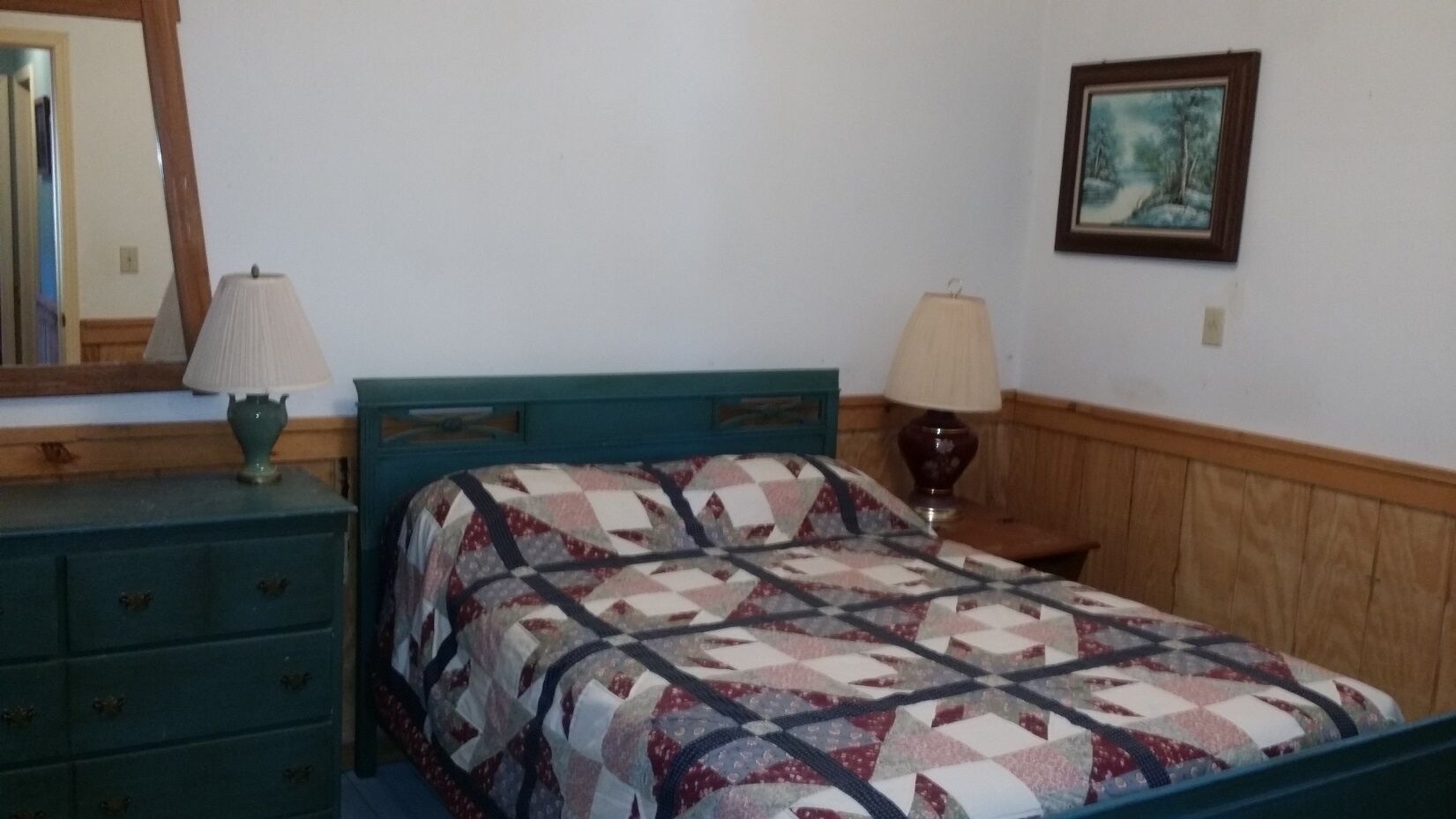 Une chambre à coucher comprenant un lit, deux tables de chevet, une commode, un miroir et un tableau encadré accroché au mur.