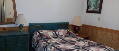 Une chambre à coucher comprenant un lit, deux tables de chevet, une commode, un miroir et un tableau encadré accroché au mur.