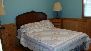 A bedroom with a wooden headboard, a quilted bedspread, a nightstand with a lamp, and a dresser. - Getaway Cabin next door to Maramec Spring Park & Meramec River Trophy Trout (St James)