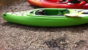 Kayaks lined up on a gravel shore by a calm river with dense forest in the background. - Getaway Cabin next door to Maramec Spring Park & Meramec River Trophy Trout (St James)
