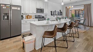 A modern kitchen with white cabinetry, a stainless steel refrigerator, a built-in microwave, and a large island with bar stools.