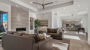 A spacious living room with a fireplace, leather sofas, and a dining area with a kitchen in the background.