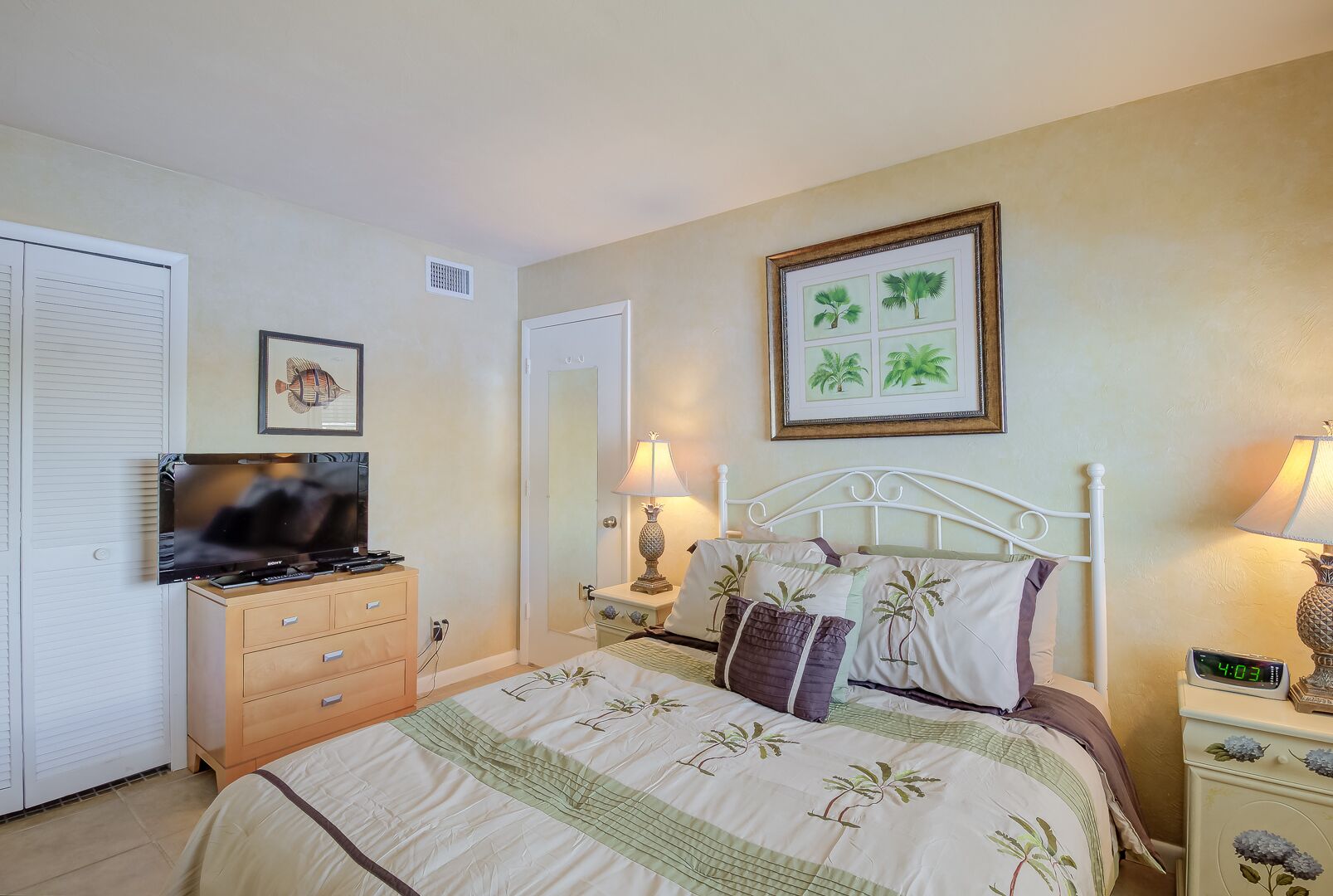 Une chambre à coucher avec un lit, une télévision, une commode et une table de chevet avec une lampe.