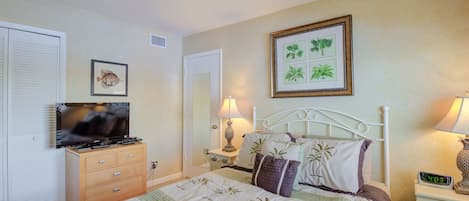 Une chambre à coucher avec un lit, une télévision, une commode et une table de chevet avec une lampe.