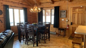 Interior de una cabaña de madera con una mesa de comedor, sillas, un sofá de cuero y una araña.