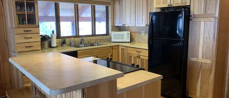 Una cocina con armarios de madera, un refrigerador negro, un microondas y una ventana con persianas.