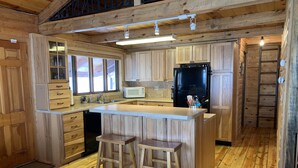 Una cocina tipo cabaña de madera con una isla central, taburetes de bar, un refrigerador, un microondas y armarios de madera.