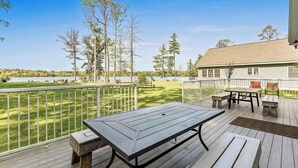 Eine Terrasse mit Tisch und Bänken mit Blick auf einen See, umgeben von Bäumen und einem Haus.