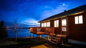 Ein Holzhaus mit einer Terrasse, großen Fenstern und Seeblick in der Nacht.