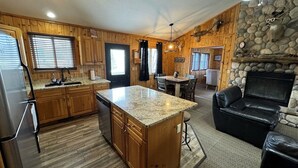 Eine Küche mit Holzausstattung, einer Kochinsel mit Granitplatte, einem Kamin aus Naturstein und einem Essbereich mit Tisch und Stühlen.