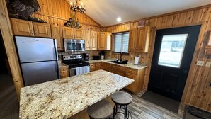 Eine Küche mit Holzausstattung, einer Arbeitsplatte aus Granit, einem Kühlschrank, einem Backofen, einer Mikrowelle und einem Spülbecken.
