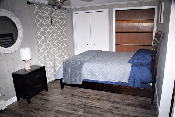 Een slaapkamer met een bed, nachtkastje, kledingkast en spiegel.