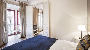 Une chambre d’hôtel avec un lit, une télévision, une lampe et un balcon équipé d’une chaise.