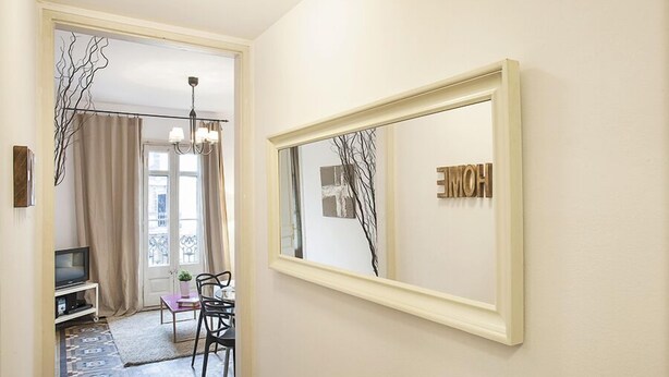 Un couloir avec un miroir, un téléviseur, un coin repas et un tapis à motifs.