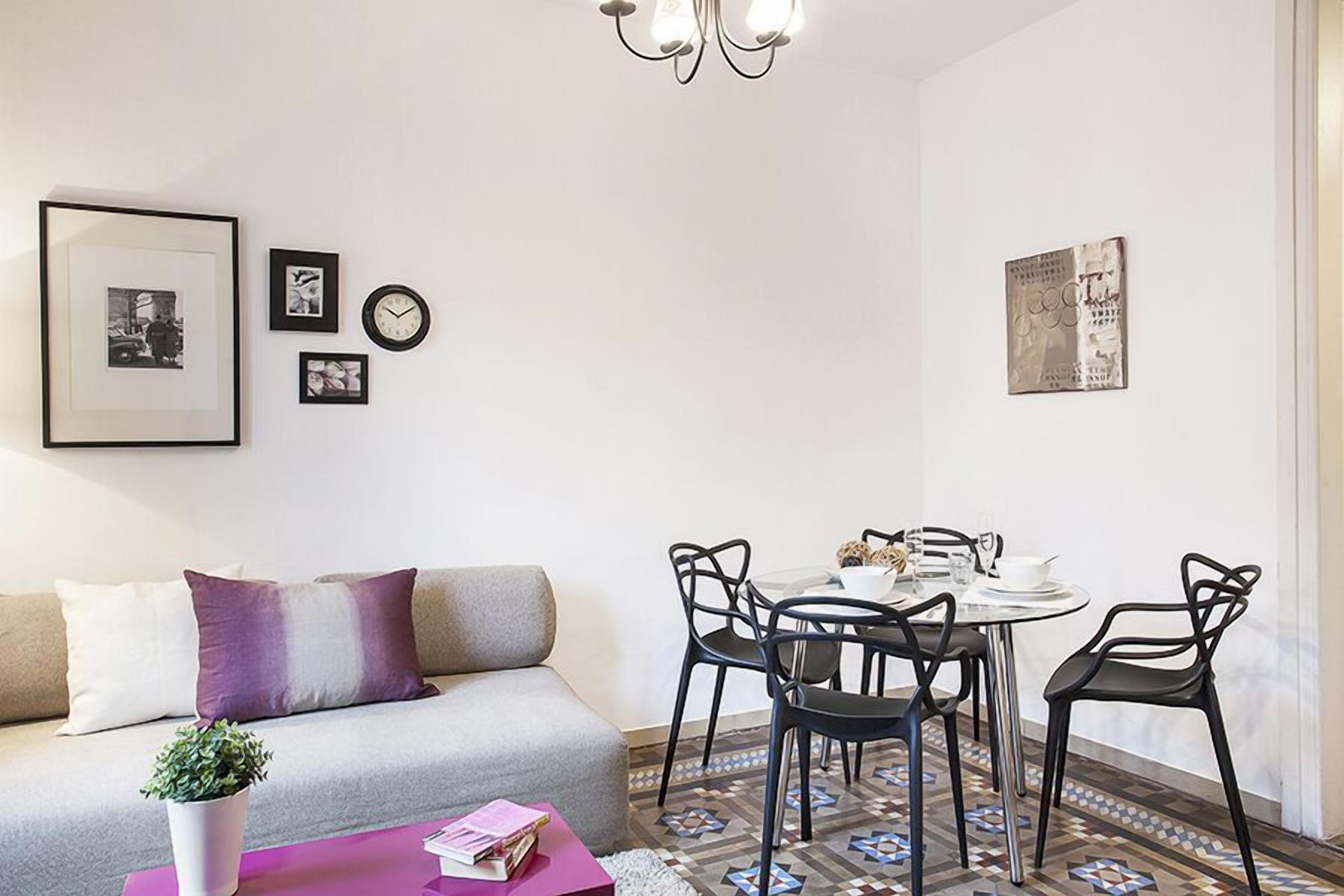 Een moderne woonkamer met een bank, een salontafel met boeken, een eettafel met stoelen en een vloer met een patroon.