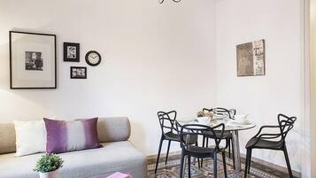 Een moderne woonkamer met een bank, een salontafel met boeken, een eettafel met stoelen en een vloer met een patroon.
