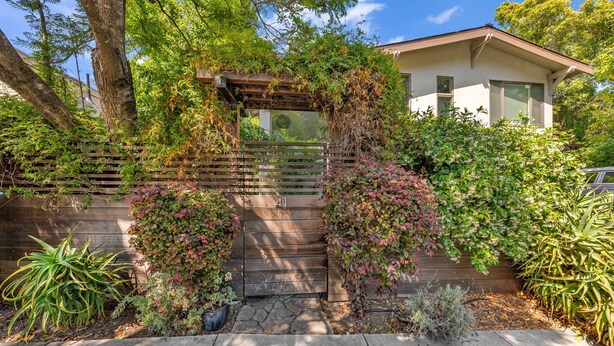 A house with a wooden fence, a gate, and a variety of plants.