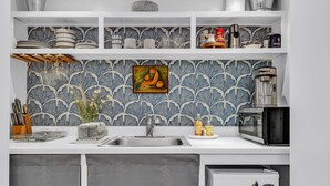 A kitchen with a patterned backsplash, a sink, a microwave, and a refrigerator.