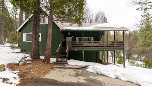 Une cabane verte dotée d’un porche abrité et d’un escalier menant à l’entrée.