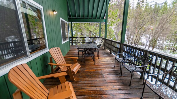 Une terrasse en bois, agrémentée de chaises Adirondack et d’une table, le tout entouré d’une rambarde verte.
