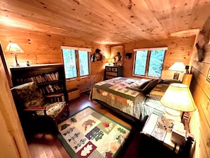 Un dormitorio de cabaña acogedor con cama, una silla, una estantería y un escritorio.