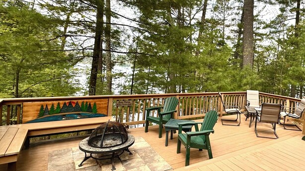 A wooden deck with a fire pit, green chairs, and a bench. - Lakeside Cottage in the Pines with Huge Deck, 40-foot Dock, and Sunset Views (Hazelhurst)