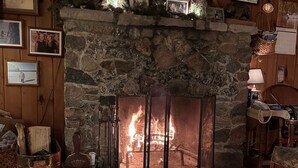 A cozy room with a stone fireplace, framed pictures on the walls, and a wooden ceiling. - Lakeside Cottage in the Pines with Huge Deck, 40-foot Dock, and Sunset Views (Hazelhurst)